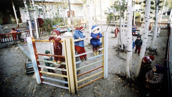 Воспитанники яслей-сада во время прогулки с воспитателем на игровой площадке, находящейся на опушке леса