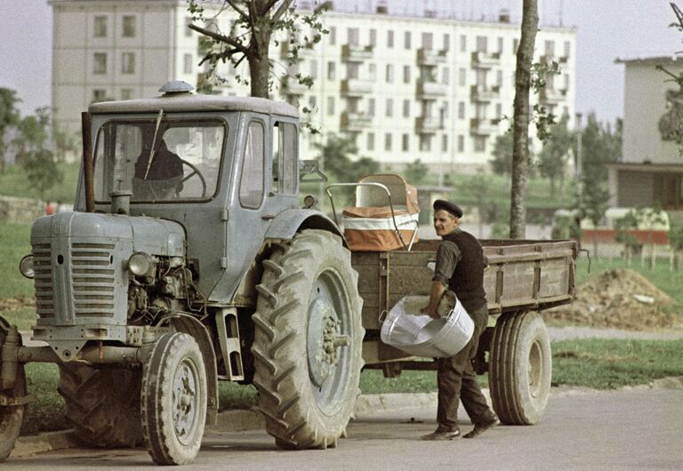 Молодой папа грузит на прицеп трактора детские вещи