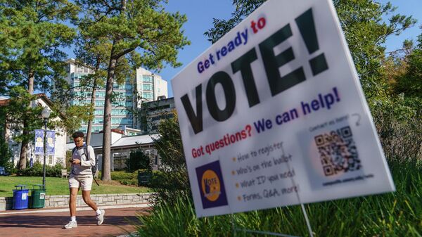 Молодой человек проходит мимо информационного знака о голосовании в кампусе Университета Эмори в Атланте, штат Джорджия