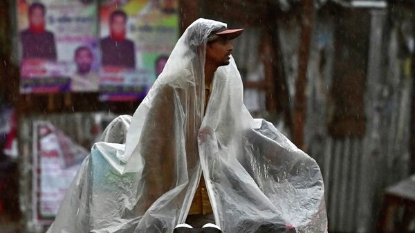 Водитель рикши защищается от дождя, ожидая пассажиров на улице в Фаридпуре, Бангладеш