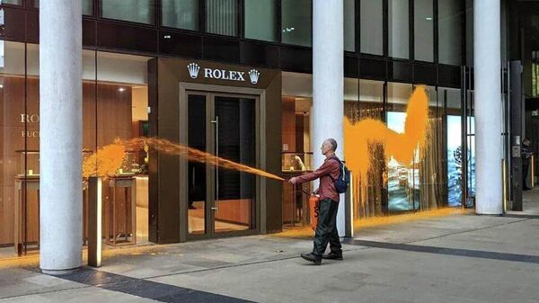 Активист экологического движения Just Stop Oil распыляет оранжевую краску из огнетушителя на фасад бутика Rolex в Лондоне