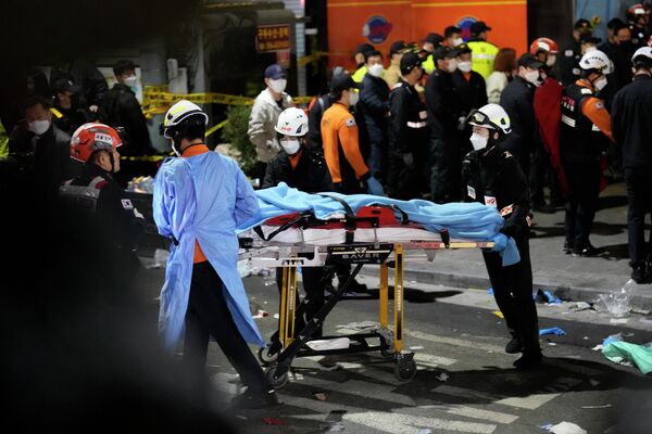 Спасатели несут пострадавшего на улице рядом с местом происшествия в Сеуле, где произошла давка