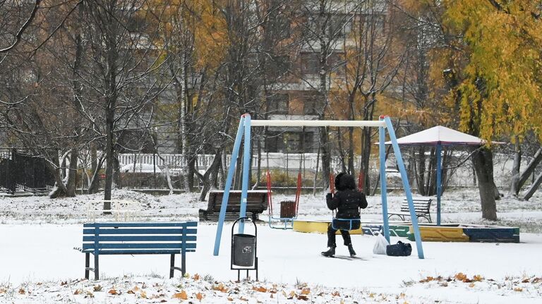 Девочка качается на качелях в заснеженном сквере на Ленинском проспекте в Москве