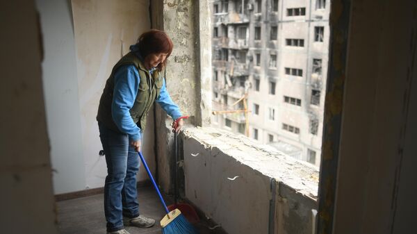 Жительница Мариуполя убирает мусор в квартире одного из разрушенных домов