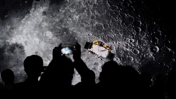 Зрители фотографируют экран с видео о китайском лунном зонде Чанъэ-5 на мероприятии, посвященном подробностям международного доступа к лунным образцам, собранным зондом, в Пекине
