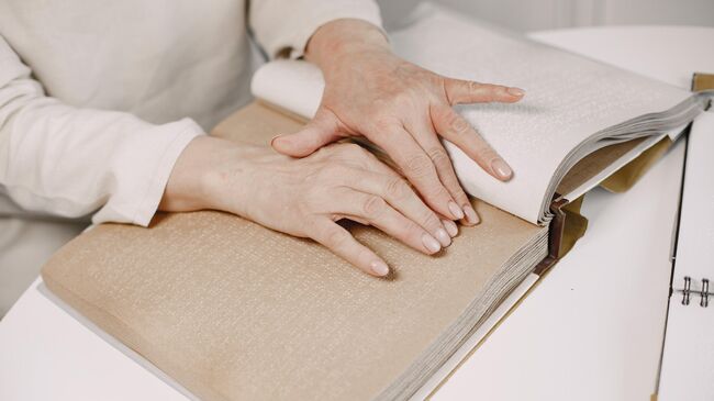 Женщина читает книгу при помощи шрифта Брайля