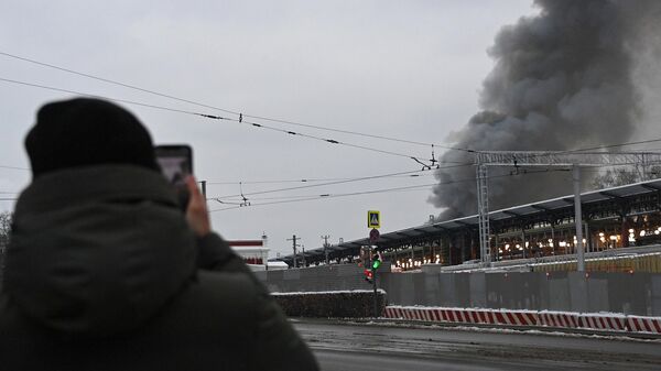 Мужчина снимает на свой телефон дым от пожара в районе Комсомольской площади