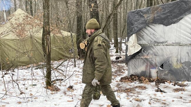 Боец на позициях артиллеристов несет дрова в полевую баню