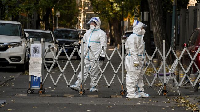 Сотрудники службы безопасности охраняют вход в жилой район в Пекине, закрытый из-за ограничений, связанных с коронавирусом