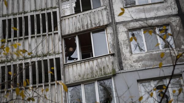 Женщина стоит около разбитого окна жилого дома в Херсоне