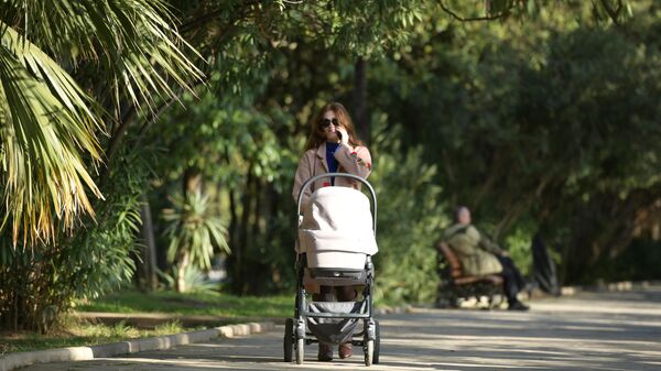 Женщина с коляской идет по аллее на набережной в городе Сухум