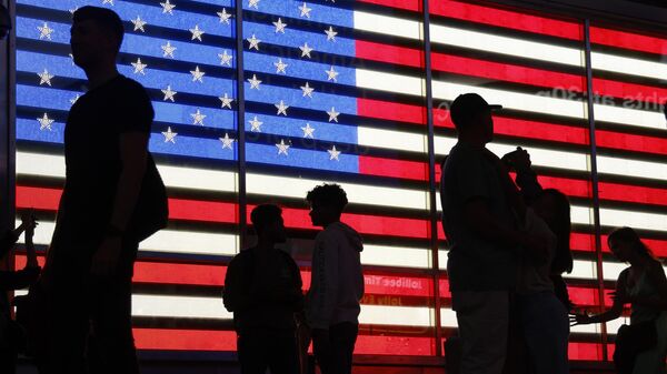 Люди на фоне флага США на площади Таймс-сквер в Нью-Йорке
