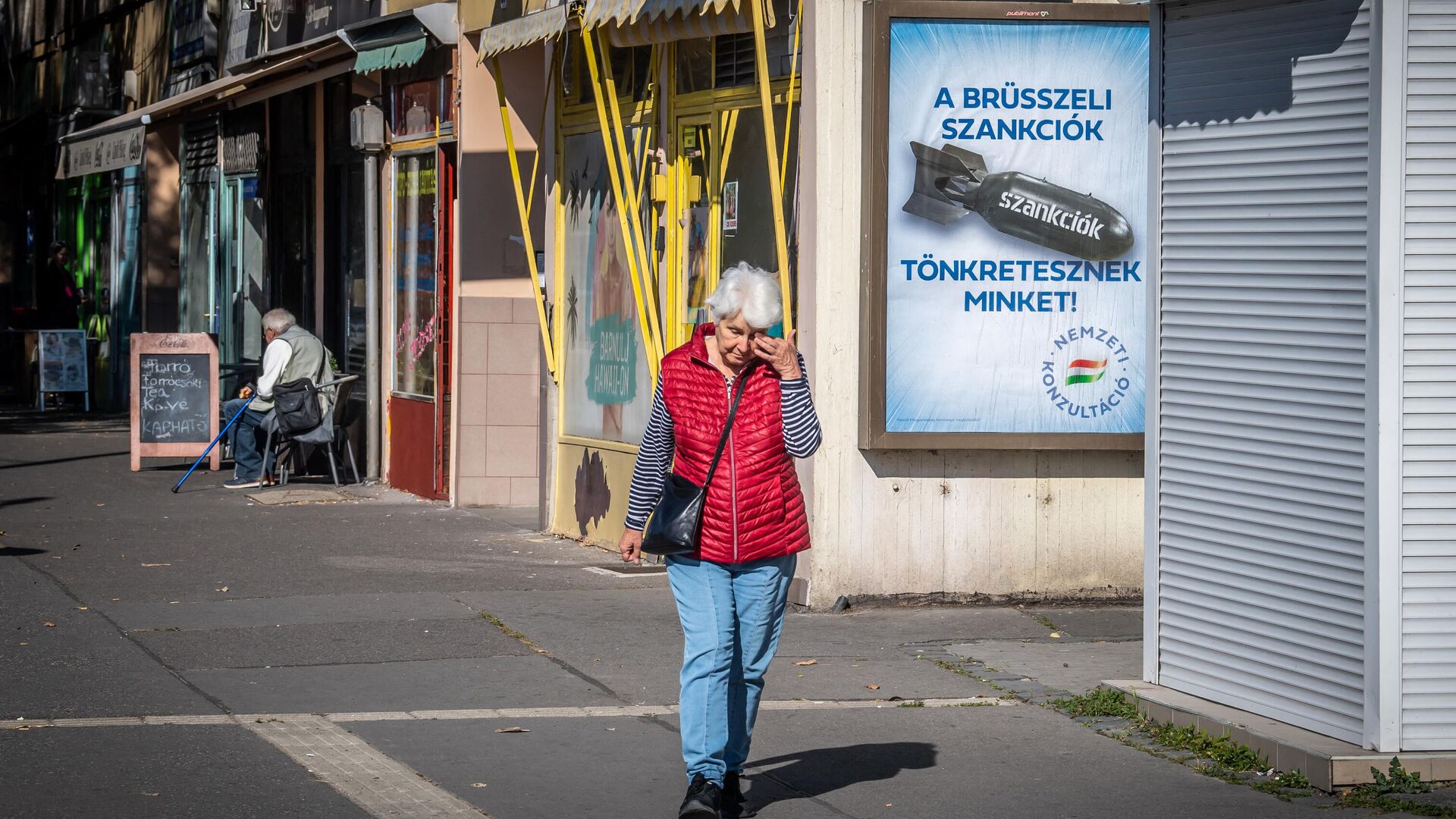 Женщина проходит мимо плаката с надписью Нас наказывают санкции Брюсселя на улице Будапешта, Венгрия - РИА Новости, 1920, 08.12.2022