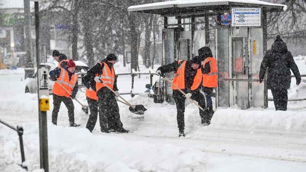 Работники коммунальной службы чистят от снега остановку московского городского транспорта. 18 декабря 2022