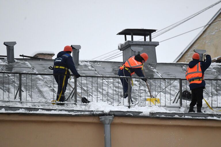 Сотрудники коммунальной службы во время уборки снега с крыши дома в Москве