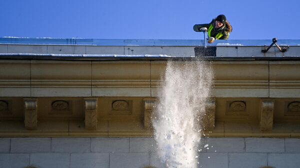 Сотрудник коммунальной службы чистит от снега крышу здания в центре Москвы