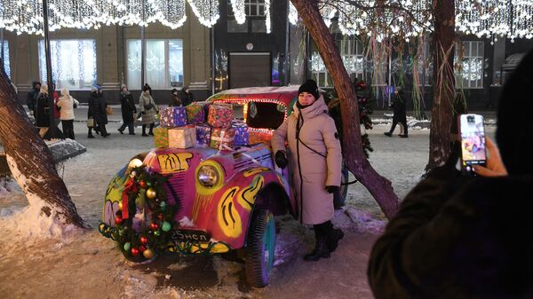 Женщина фотографируется около декоративного автомобиля в новогоднем оформлении на улице Ленина в Новосибирске