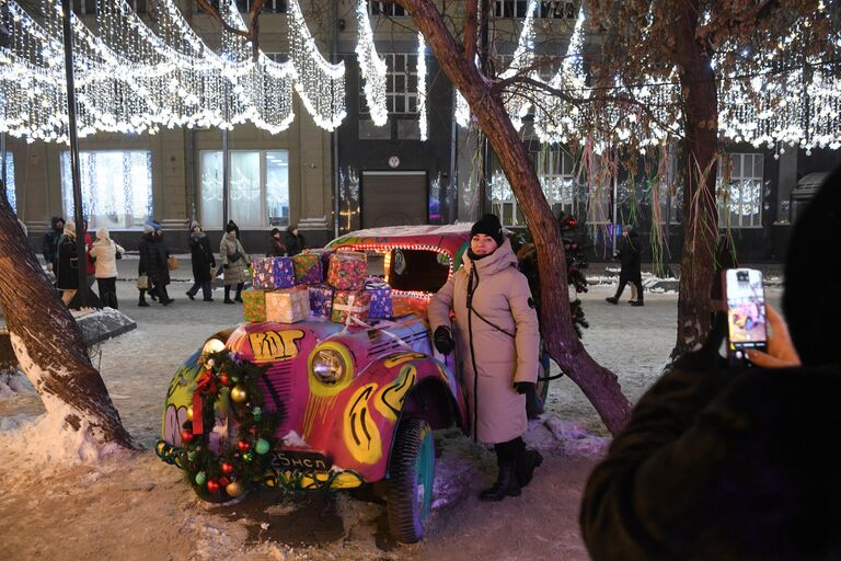 Женщина фотографируется около декоративного автомобиля в новогоднем оформлении на улице Ленина в Новосибирске