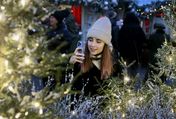 Посетительница фотографирует украшенную ёлку на фестивале Путешествие в Рождество на Манежной площади в Москве