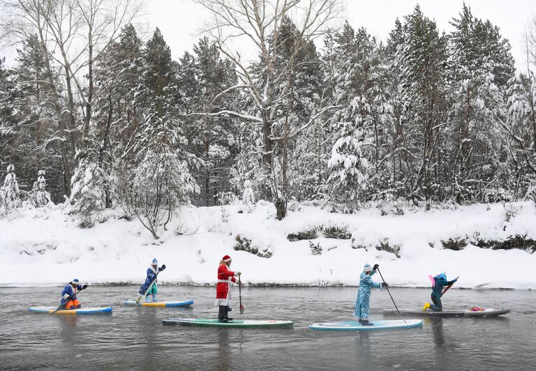 Спортсмены группы сапсерфинга SUP-Novosibirsk участвуют в новогоднем заплыве по незамерзающей реке недалеко от Новосибирска