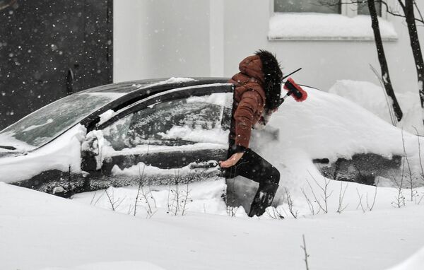 Женщина чистит от снега автомобиль
