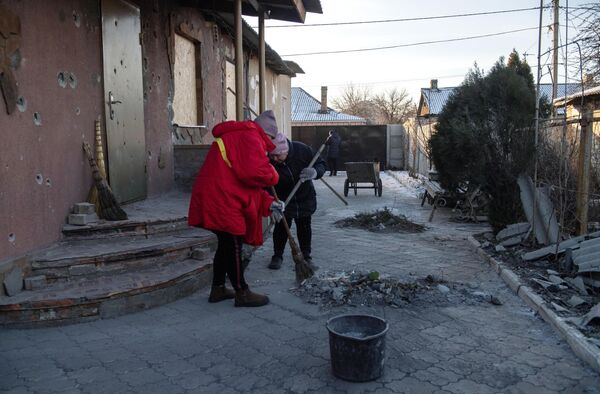 Местные жительницы убираются во дворе дома, пострадавшего в результате обстрела в Петровском районе Донецка