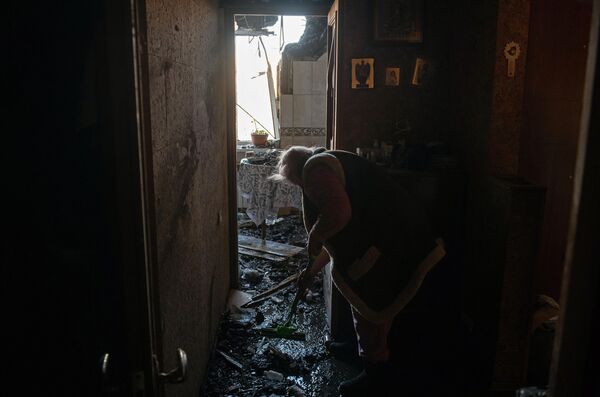 Местная жительница убирается в квартире, пострадавшей в результате обстрела в Петровском районе Донецка