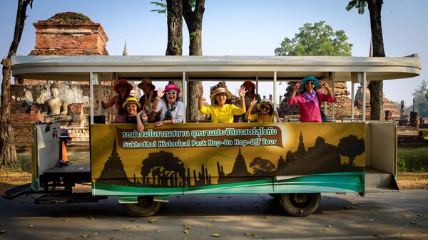 Туристы машут из электрического экскурсионного автобуса Hop-on Hop-off в историческом парке Сукхотай