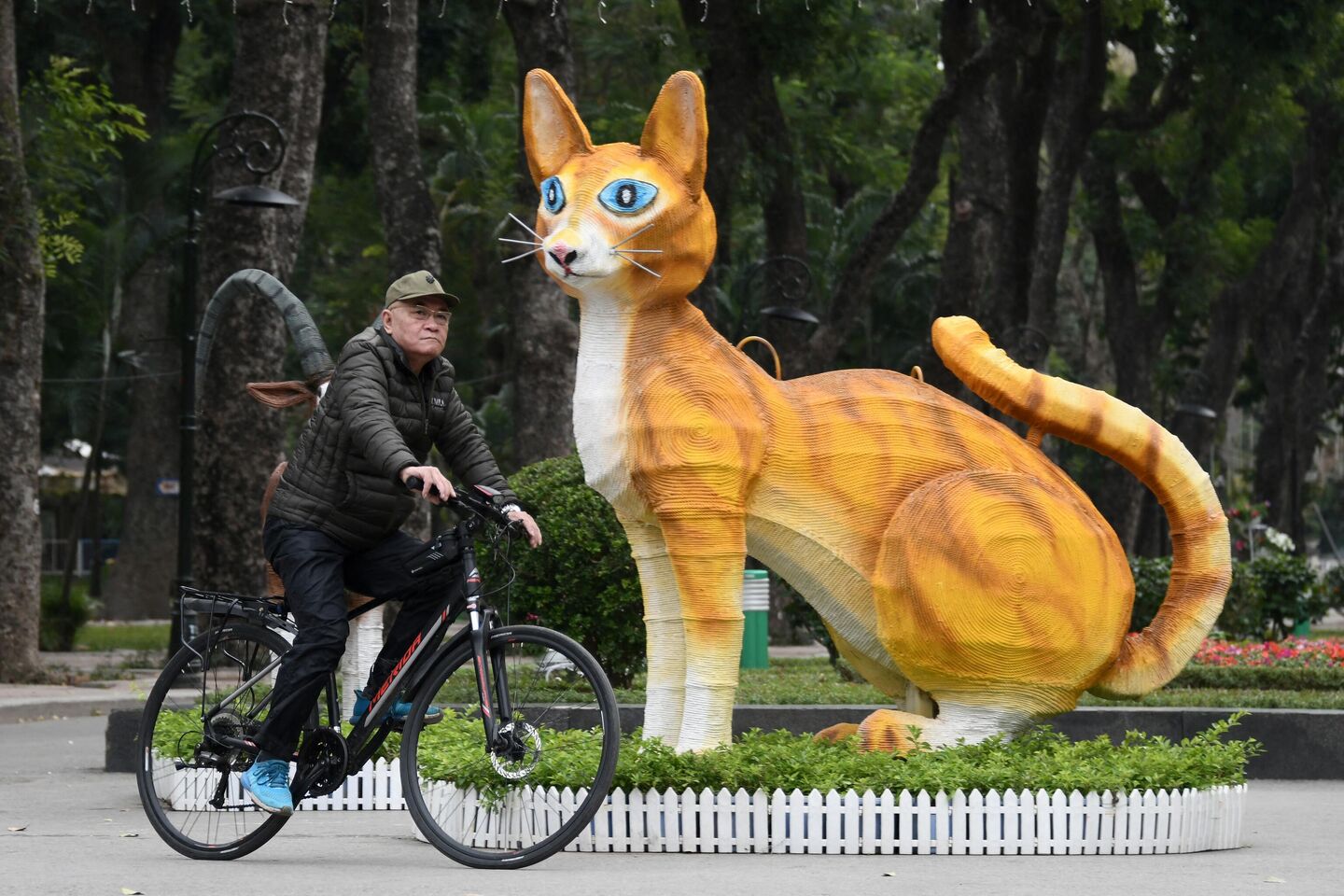 Мужчина проезжает возле статуи кошки в парке Thong Nhat Park в Ханое, Вьетнам Мужчина проезжает возле статуи кошки в парке Thong Nhat Park в Ханое, Вьетнам