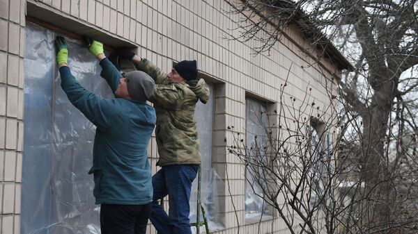 Мужчины заклеивают окна пленкой, поврежденные в результате обстрела со стороны украинских войск в Иловайске