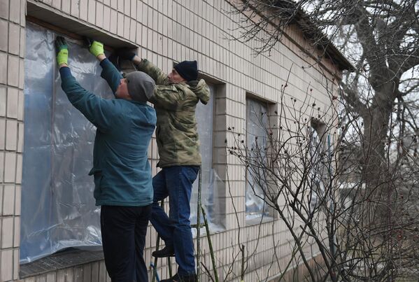 Мужчины заклеивают окна пленкой, поврежденные в результате обстрела со стороны украинских войск в Иловайске