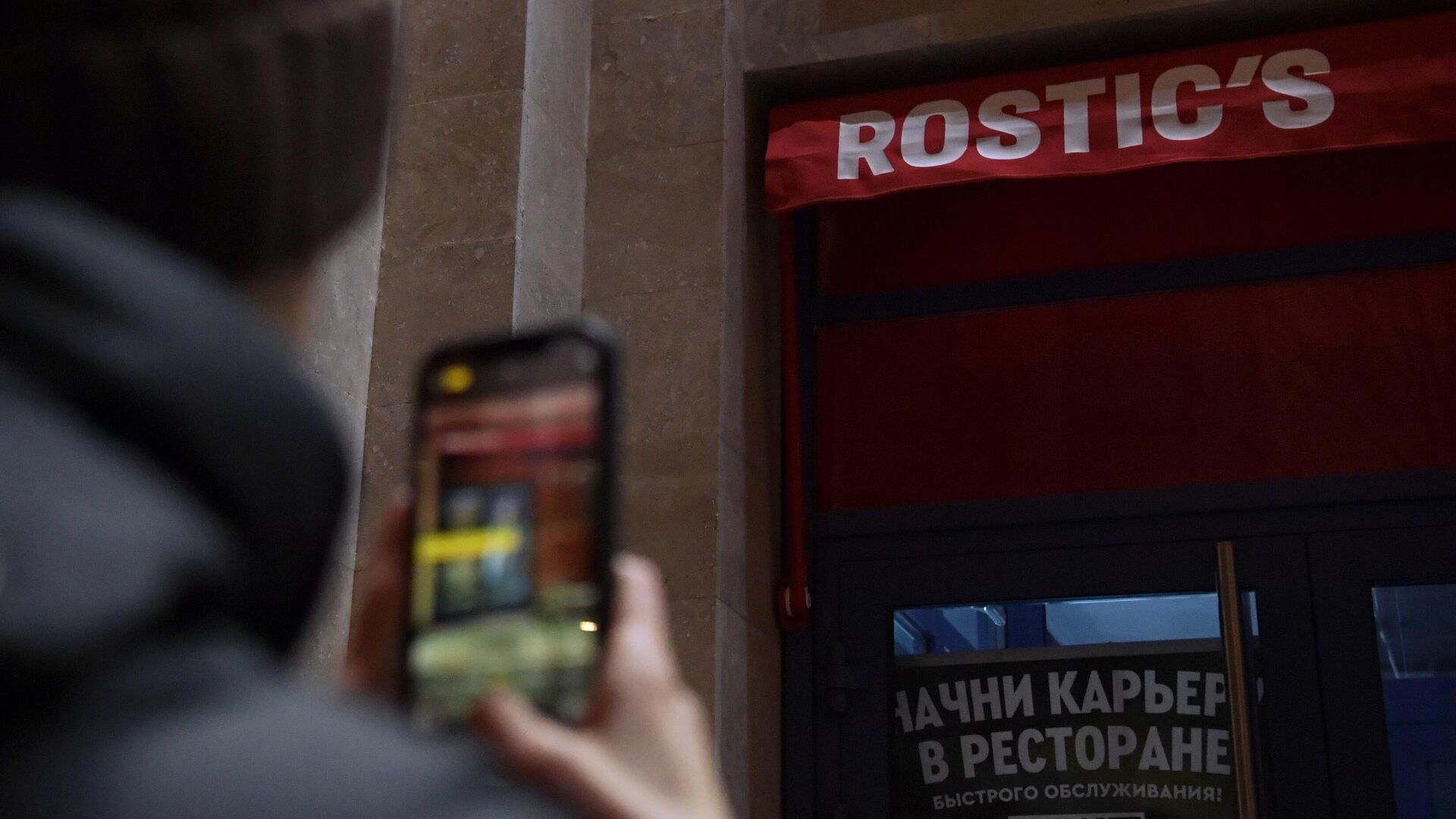 Мужчина фотографирует вывеску ресторана Rostic's недалеко от метро ВДНХ в Москве - РИА Новости, 1920, 24.01.2023
