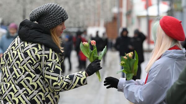 Девушка-волонтер на Никольской улице дарит женщине цветы в честь Международного женского дня