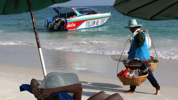 Торговец фруктами проходит мимо отдыхающих на пляже острова Ко Куди