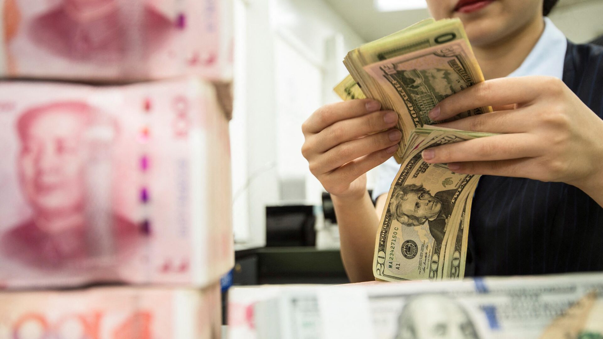 Сотрудник китайского банка пересчитывает банкноты номиналом 100 юаней и доллары США  - РИА Новости, 1920, 24.03.2023