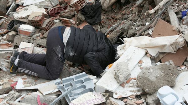 Мужчина ищет людей под завалами здания, разрушенного в результате землетрясения в турецком Диярбакыре
