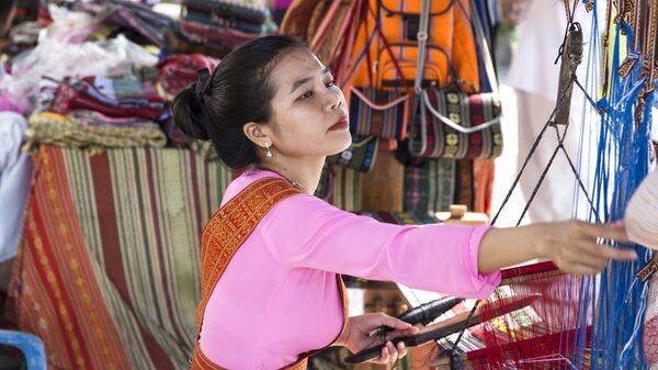 Девушка в национальном костюме работает на традиционном ручном ткацком станке в Нячанге, Вьетнам