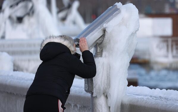 Девушка смотрит в обледеневший уличный бинокль на смотровой площадке на набережной Новороссийска