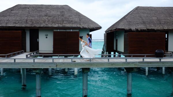 Туристы у вилл на сваях, построенных в прибрежных водах острова Велассару, Мальдивы