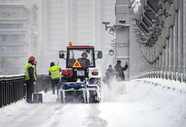Работники коммунальной службы убирают от снега пешеходную часть Крымского моста в Москве