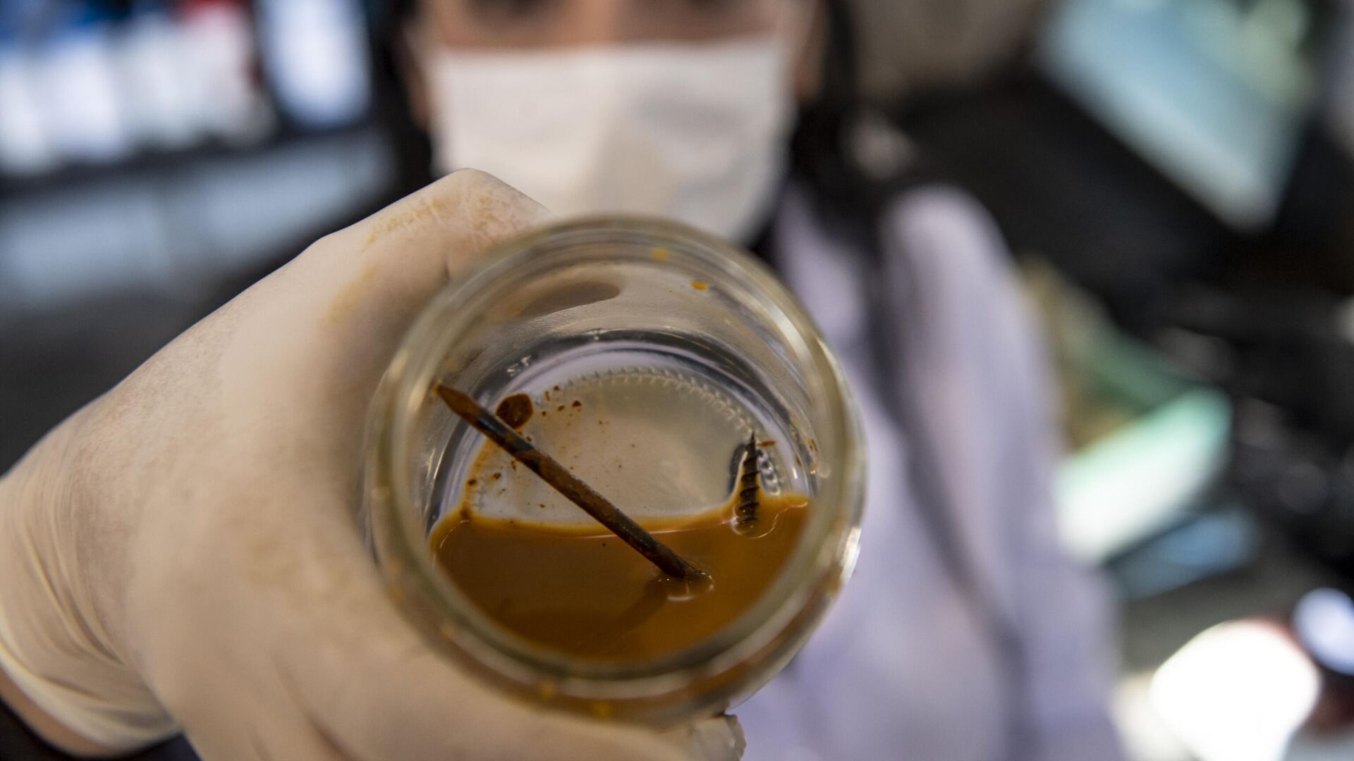Чилийский биотехнолог Надак Реалес демонстрирует гвоздь и шуруп в банке с бактериями, способными поедать металл, в своей лаборатории на горнодобывающем предприятии в Антофагасте - РИА Новости, 1920, 17.02.2023