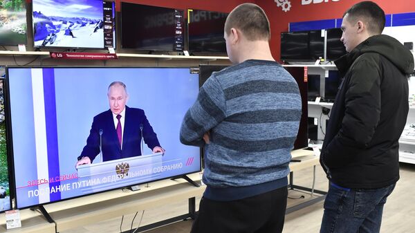 Молодые люди смотрят трансляцию ежегодного послания президента РФ Владимира Путина Федеральному Собранию в магазине техники и электроники в Симферополе