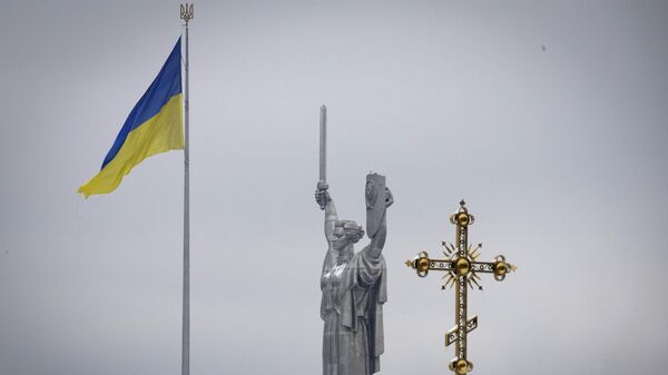 Крест монастырского комплекса Киево-Печерской лавры на фоне украинского государственного флага и монумента Родина-мать в Киеве