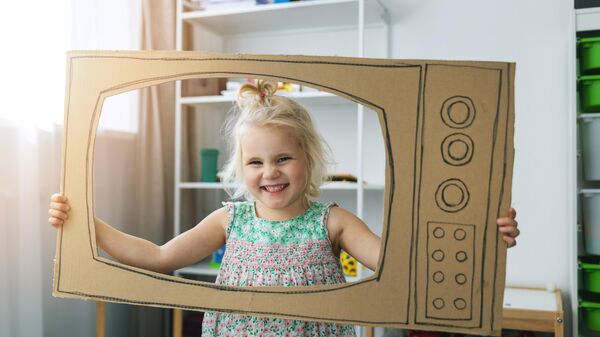 Девочка играет с вырезанным из картона телевизором 