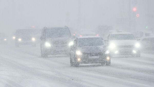 Автомобили едут по дороге во время снегопада в Москве