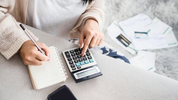 Женщина рассчитывает свои расходы по счетам с помощью калькулятора