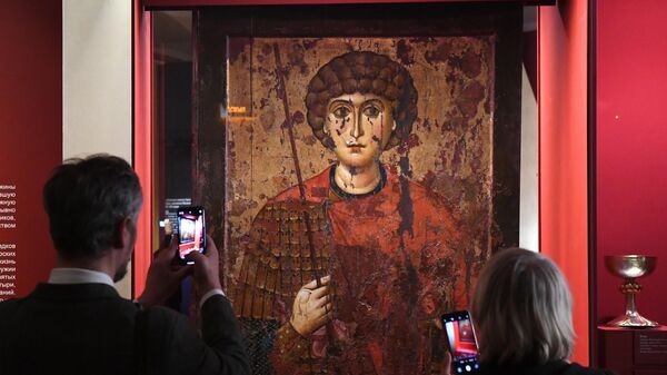 Посетители фотографируют икону с изображением Святого великомученика Георгия на выставке Небесное воинство. Образ и почитание в выставочном зале Успенской звонницы Московского Кремля