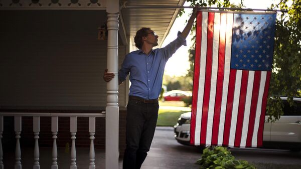 Мужчина поправляет американский флаг на крыльце своего дома
