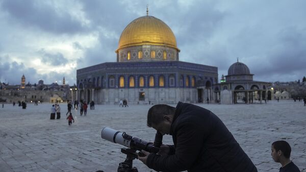 Мужчина наблюдает за Луной в телескоп рядом с мечетью Купол Скалы на Храмовой горе в Иерусалиме