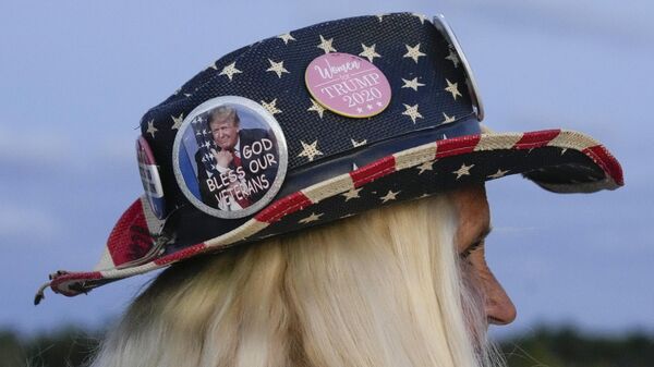 Женщина в шляпе с американским флагом и значком с изображением Дональда Трампа в знак поддержки